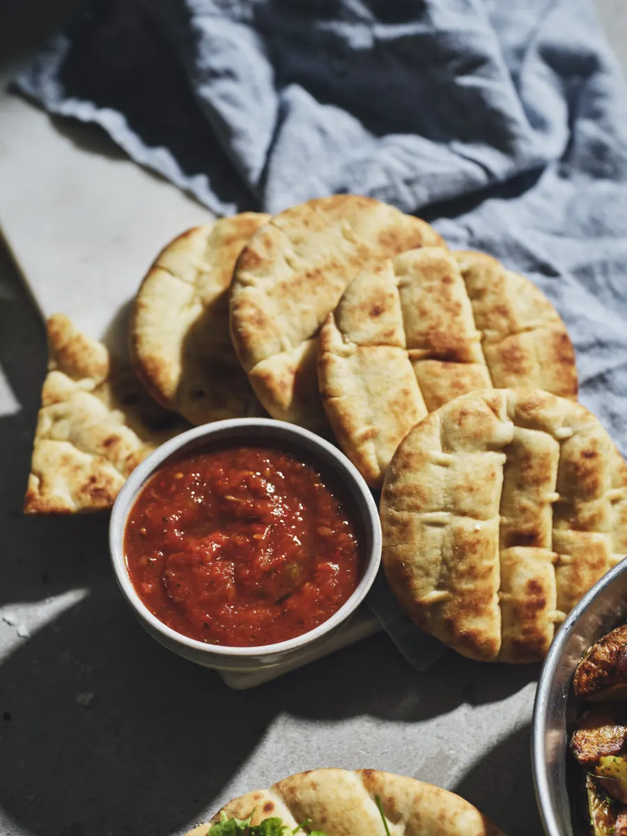 Skål med grekisk tomatsalsa bredvid en hög med grekiska minipitabröd
