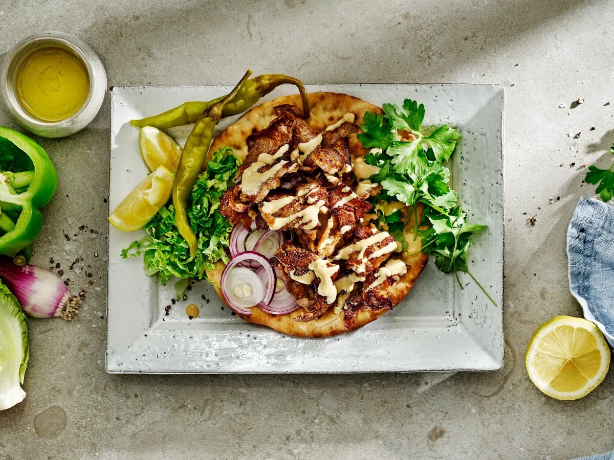 Fläskgyros på pitabröd med sås, rödlök och persilja på ett kantigt stengodsfat