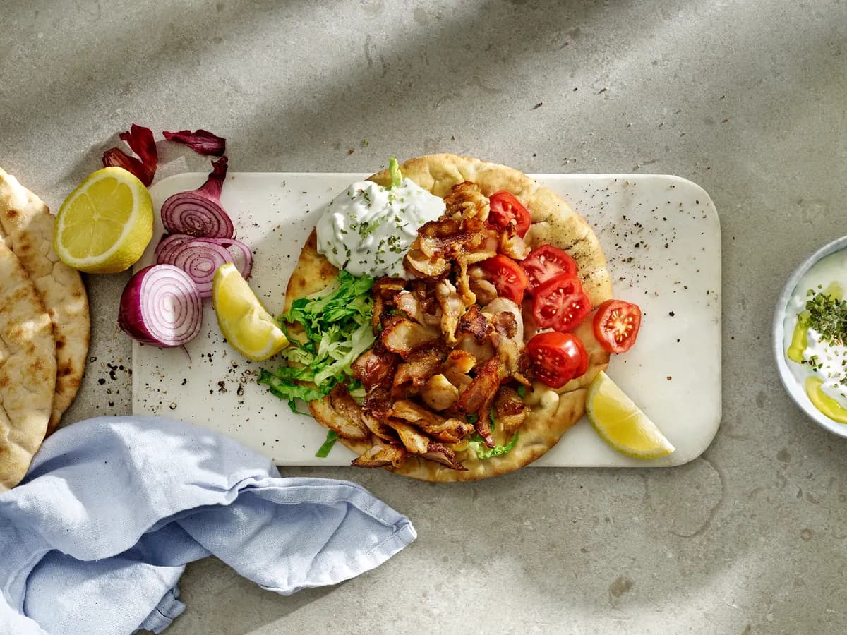 Kycklinggyros på pitabröd med tzatziki, körsbärstomater och strimlad sallad på en skärbräda