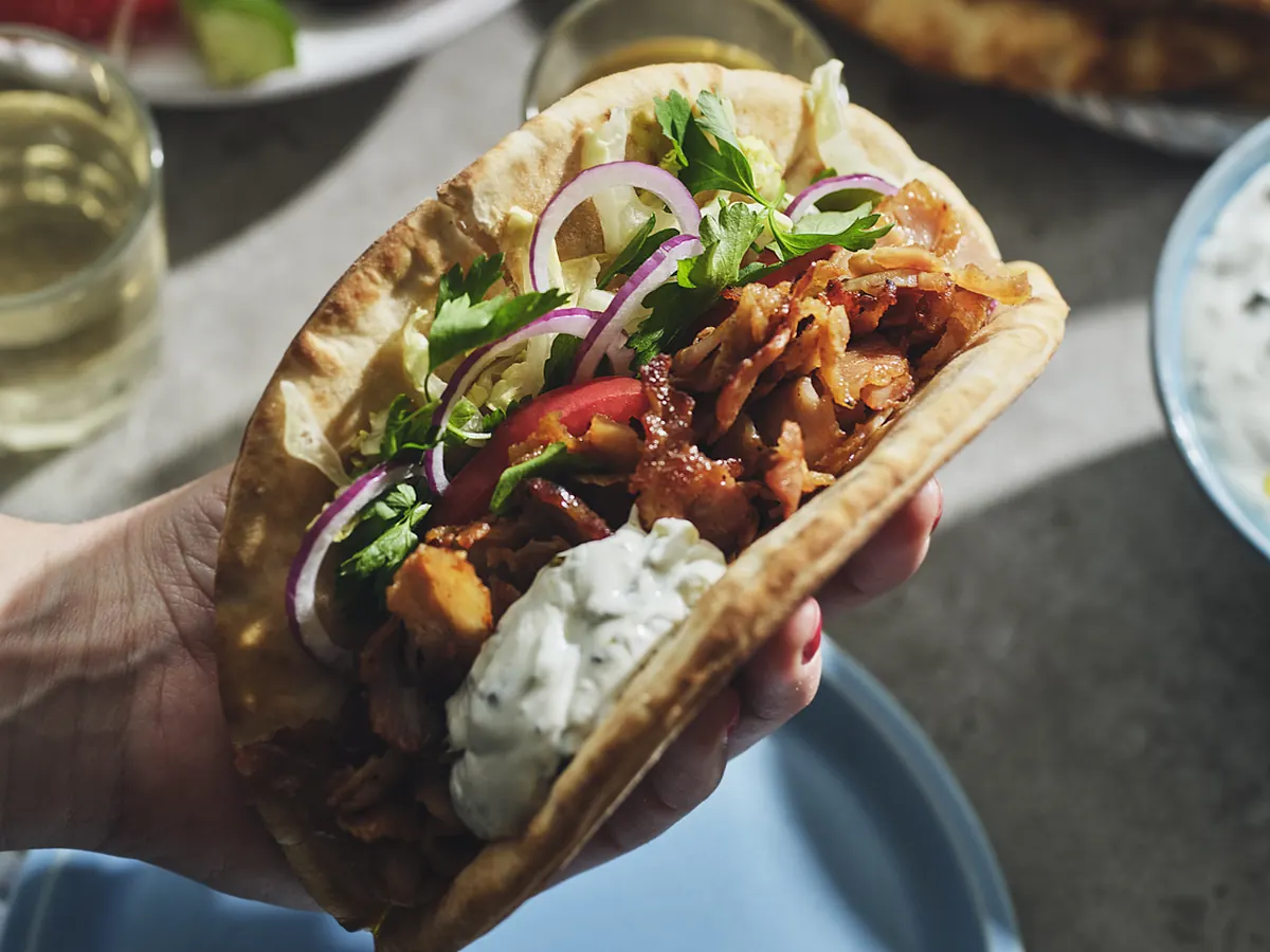 En hand som håller ett hopvikt pitabröd fyllt med gyros, tomat, rödlök och tzatziki