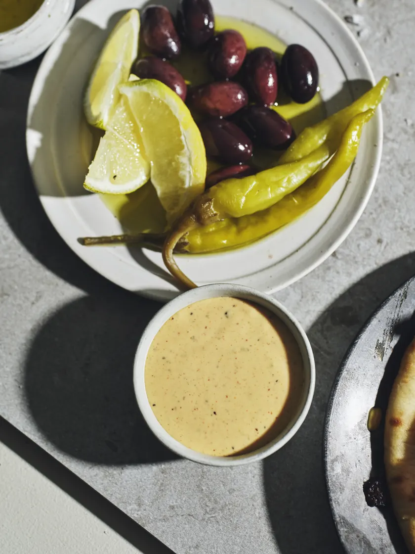 Skål med krämig gyrossås bredvid ett fat med oliver, pepperoncini och citronklyftor