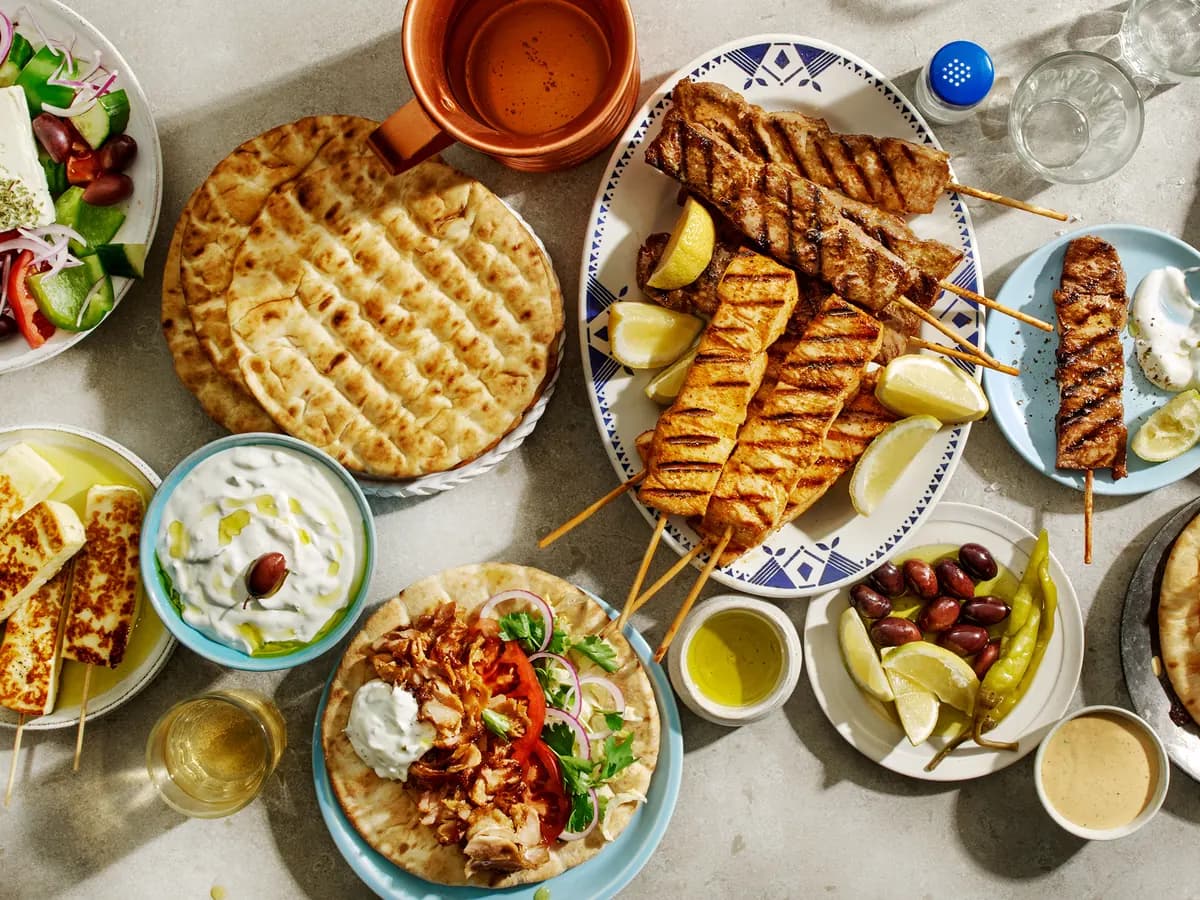 Ett dukat grekiskt bord med pitabröd, souvlaki, gyrospita, tzatziki och oliver