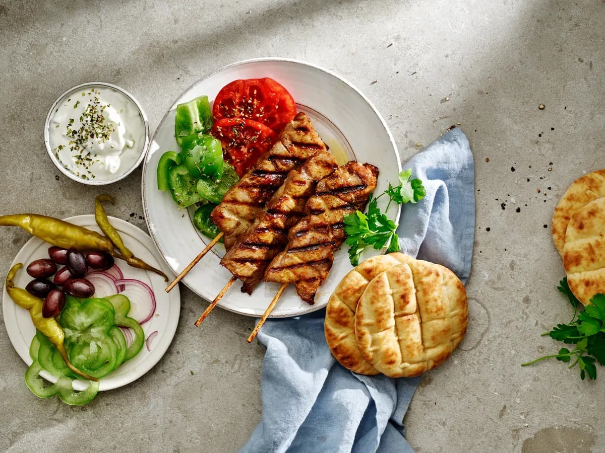 Grillade fläskspett på en tallrik med tomat, grön paprika och pitabröd bredvid